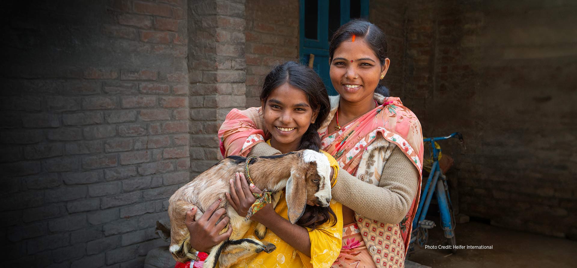 Two female livestock farmers in India smile while holding a young goat. - Zoetis Foundation - Photo Credit: Heifer International 