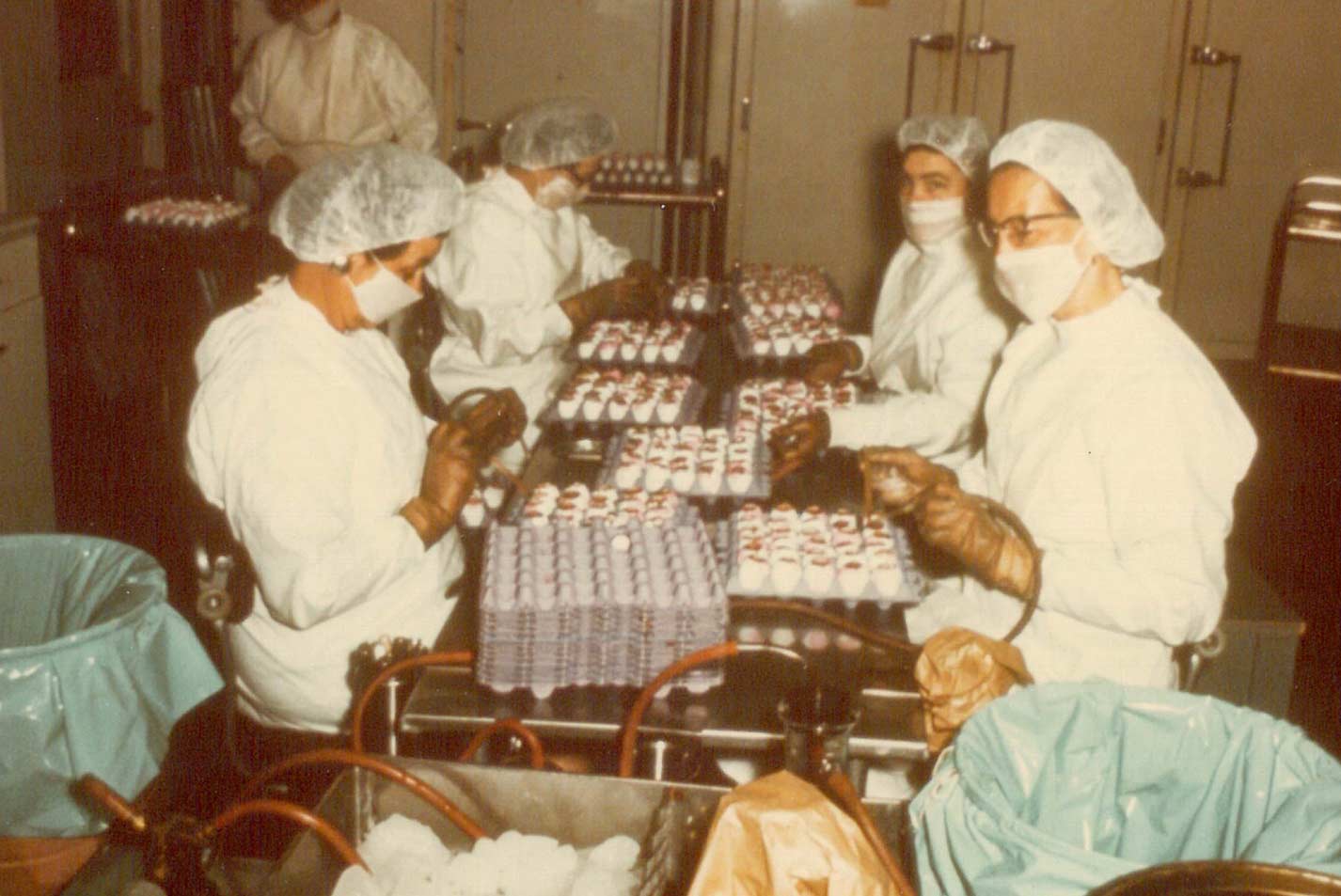 Workers in white coats, hairnets, and gloves sort eggs at a long table in a vaccine production facility - Zoetis